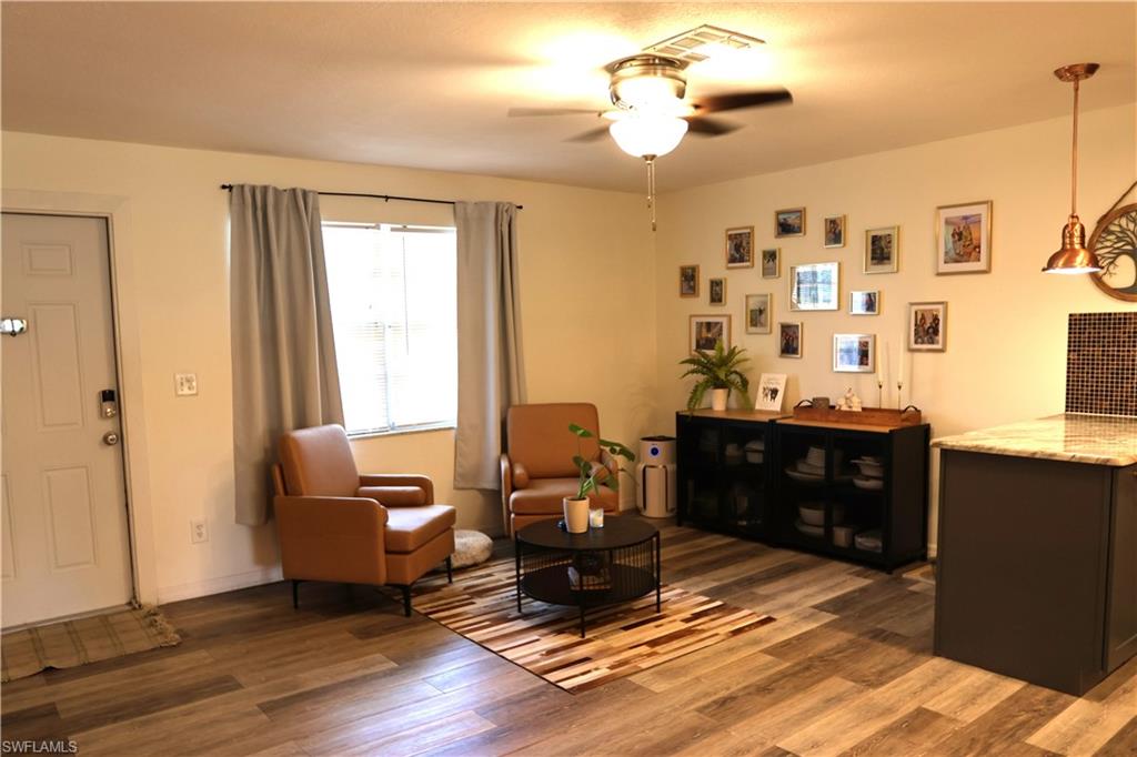 Open-concept living area featuring wood-finish flooring, a ceiling fan with integrated lighting, and a built-in storage unit
