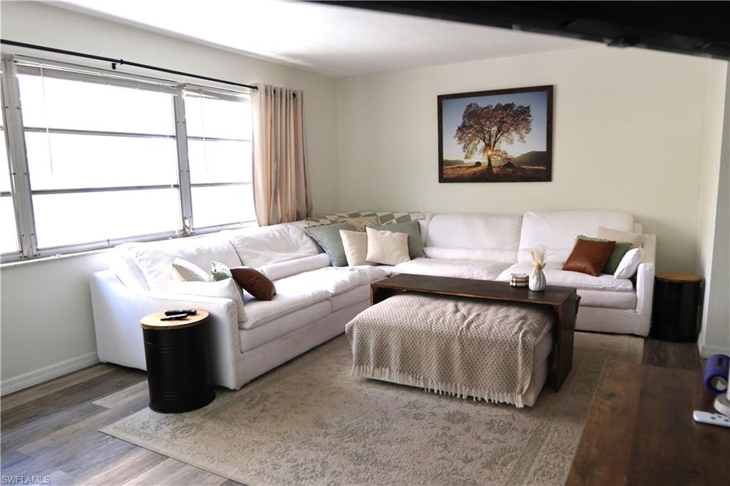 Spacious living area featuring light-toned walls, wood-finish flooring, and a large window with vertical blinds