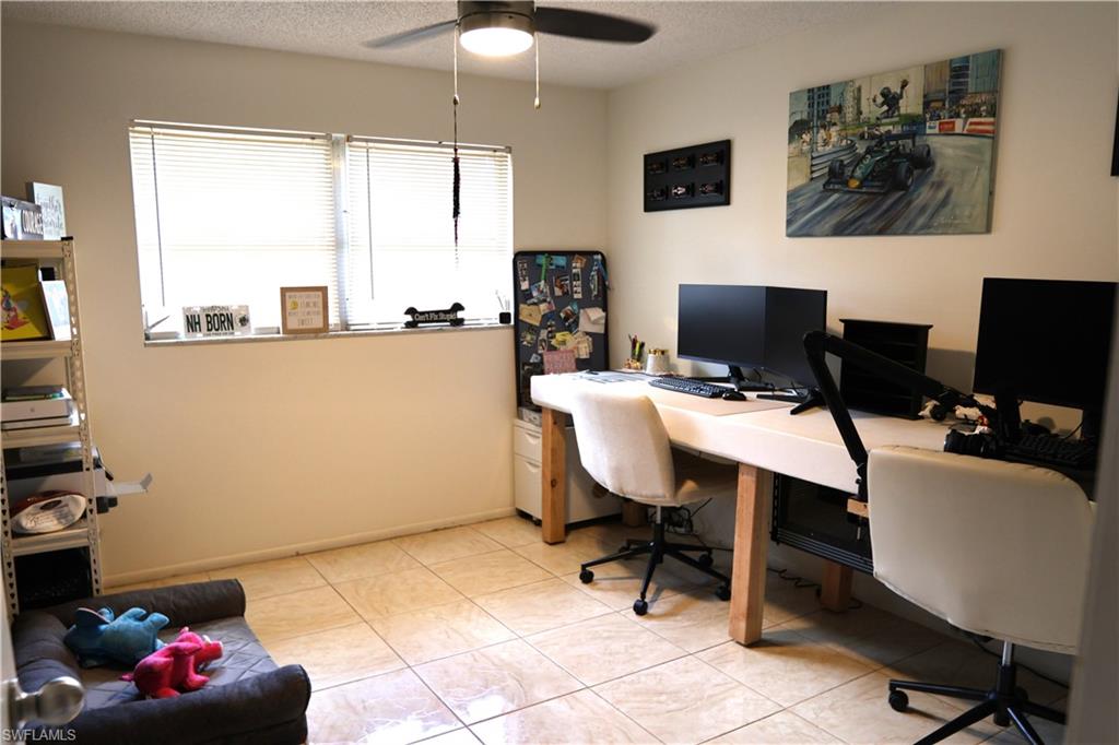 Room featuring ceramic tile flooring, a dual window with blinds, a ceiling fan with integrated lighting, and a built-in desk area