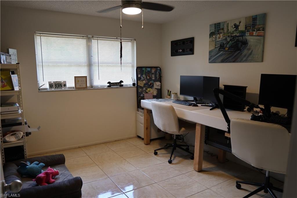 Spacious interior room featuring light-toned tile flooring, dual windows with blinds, a ceiling fan with light fixture, and neutral wall paint