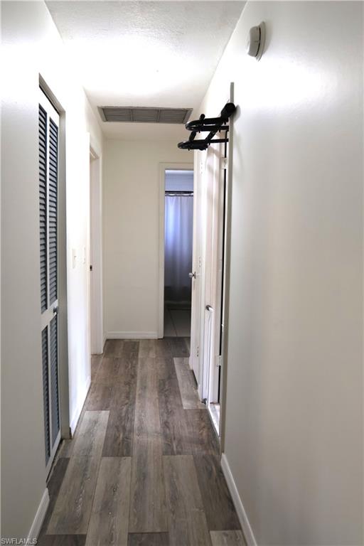 Hallway featuring wood-finish flooring, white baseboards, and a white ceiling with a rectangular air vent