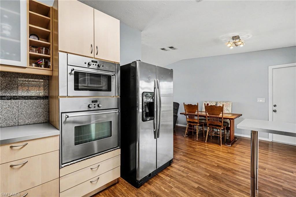 Kitchen featuring stainless steel appliances, light wood-finish cabinetry, a built-in oven, a built-in microwave, and wood-finish flooring