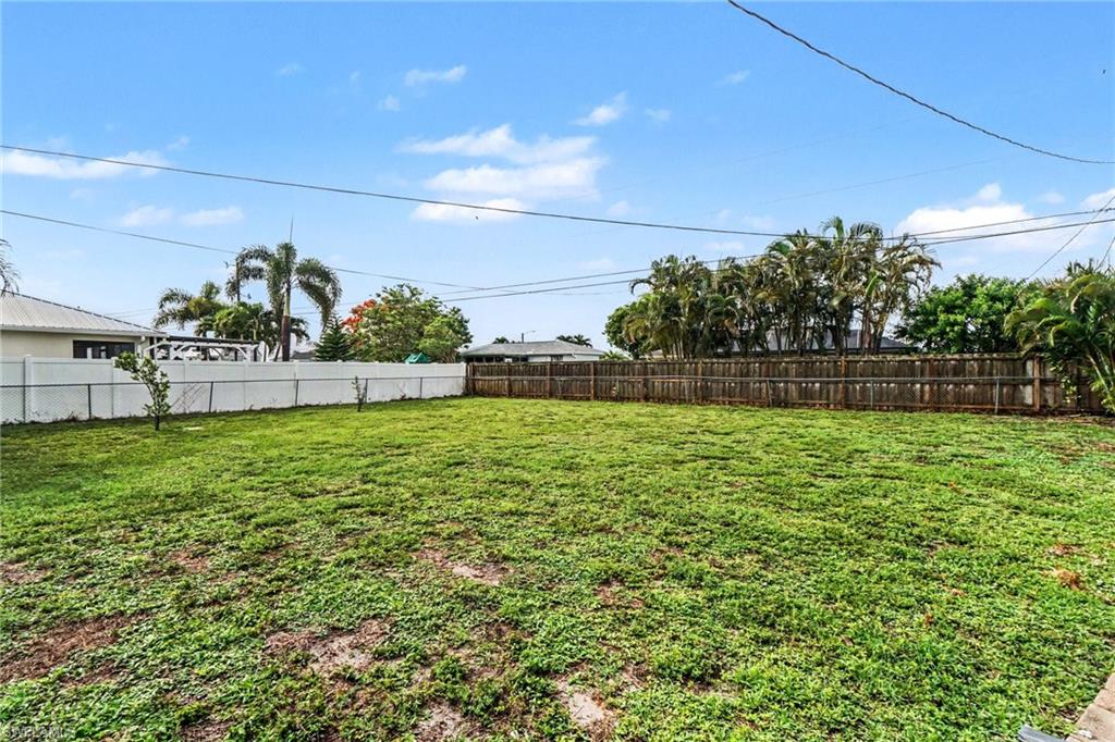 Expansive rear yard featuring green ground cover, a perimeter privacy fence, and mature palms