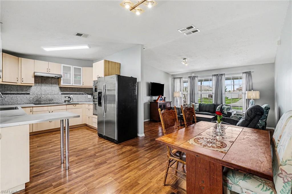 Open-concept living space featuring wood-finish flooring, a kitchen with light wood cabinetry and stainless steel appliances, and a dining area with a wood table