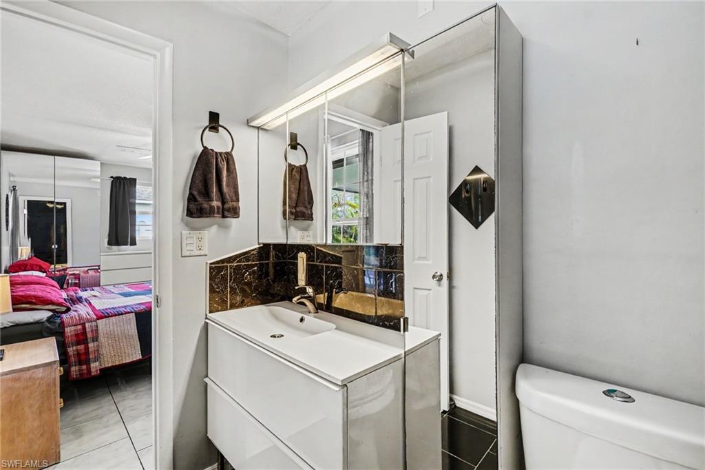 Bathroom vanity featuring a white rectangular sink with a single-handle faucet, dark tile backsplash, and a large mirrored medicine cabinet with integrated lighting