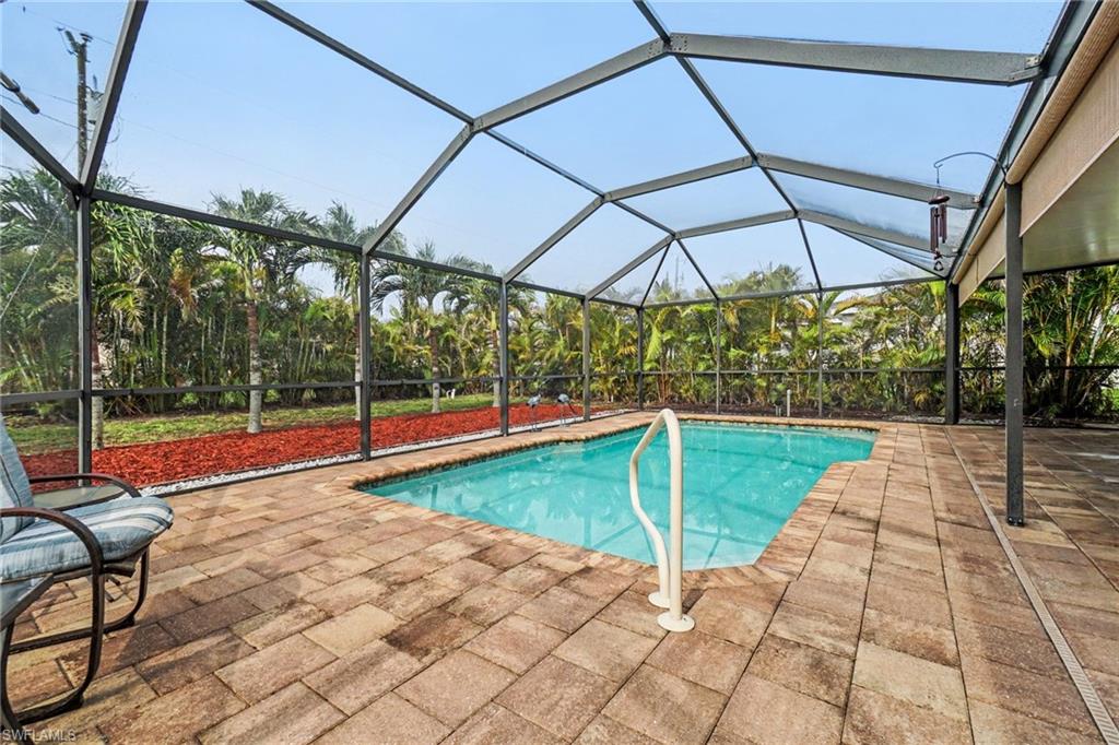 Screen-enclosed pool area featuring an in-ground swimming pool with handrail, paver decking, and a covered patio space