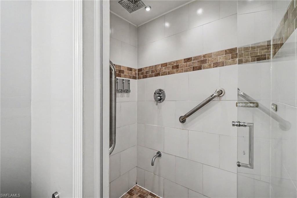 Walk-in shower featuring white tile walls with a decorative brown accent band and a coordinated brown tile floor