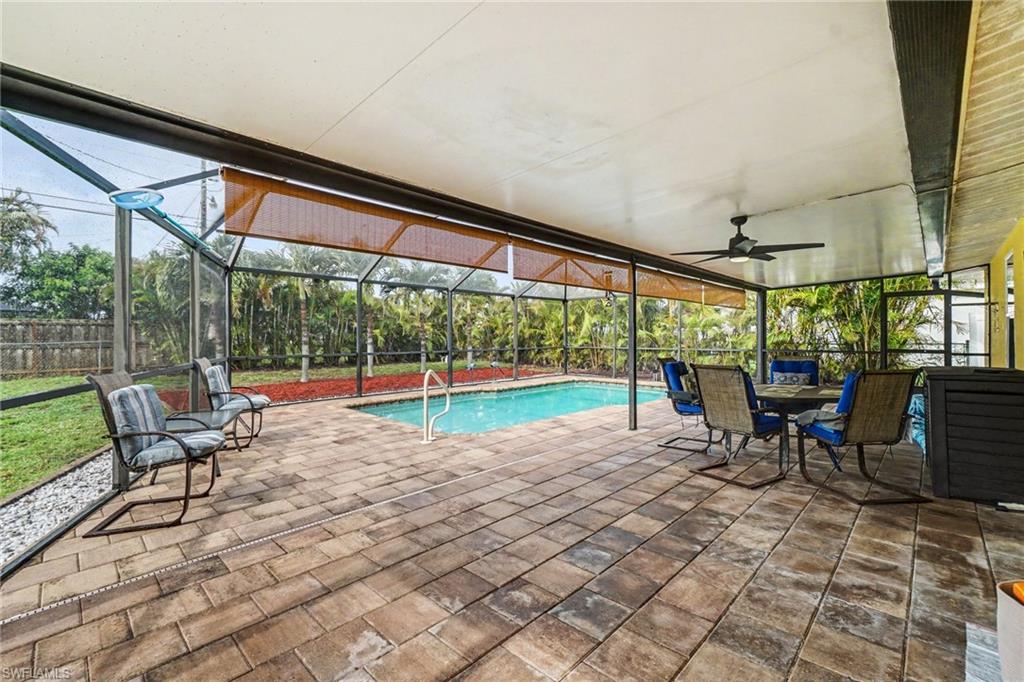 Expansive screened patio featuring a swimming pool with white handrails, paver stone decking, and a ceiling fan with integrated lighting