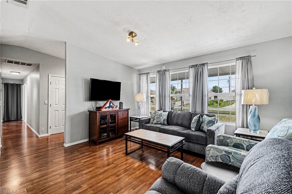 Living area featuring wood-finish flooring, light grey wall paint, and multiple windows with curtain rods