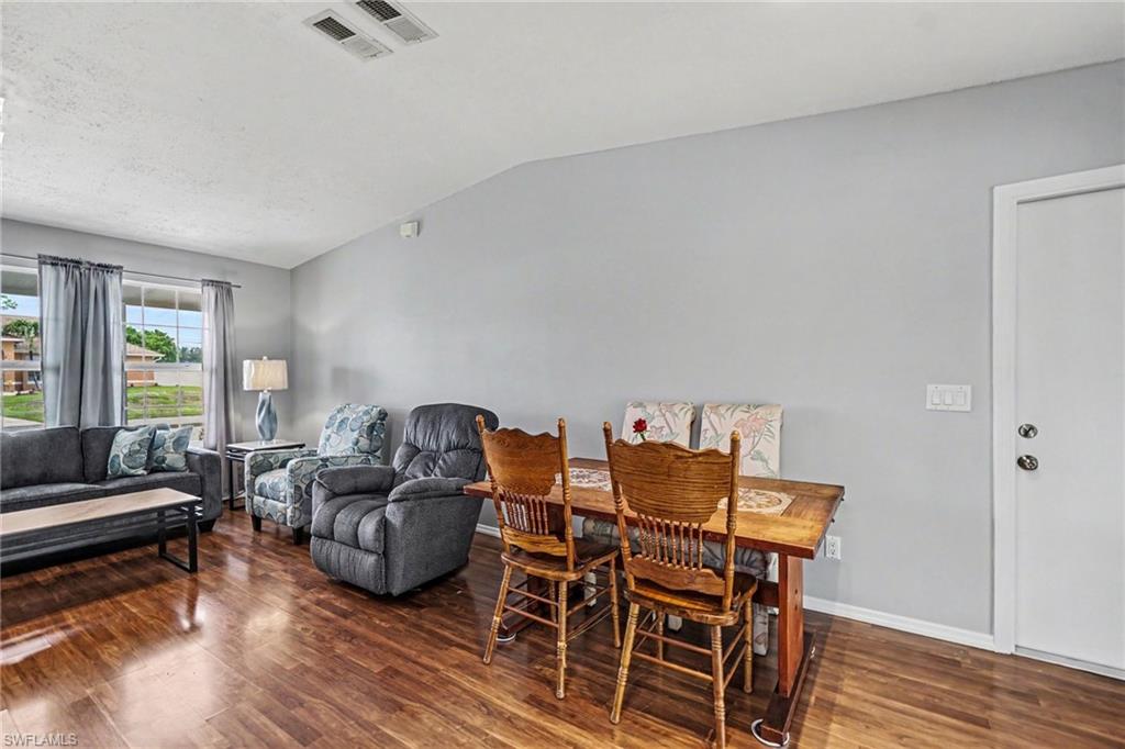 Open-concept living space featuring wood-finish flooring, a vaulted ceiling, and ample natural light from multiple windows