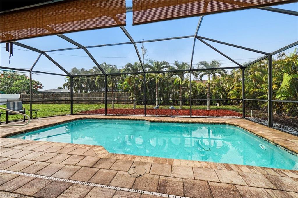 Screened-in outdoor pool featuring a paver deck, surrounding landscaping, and mature palm trees