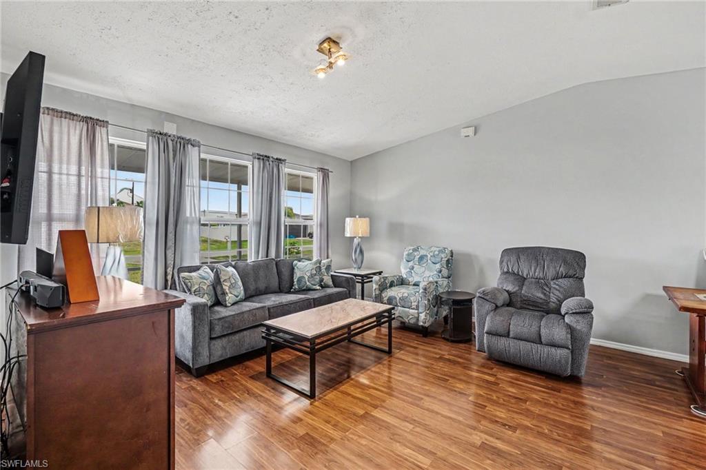 Interior living space featuring wood-finish flooring, light gray wall paint, and multiple windows with vertical blinds