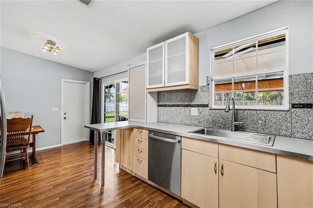 Kitchen featuring light wood-finish cabinetry, stainless steel sink, and a granite-look backsplash with decorative tile accent