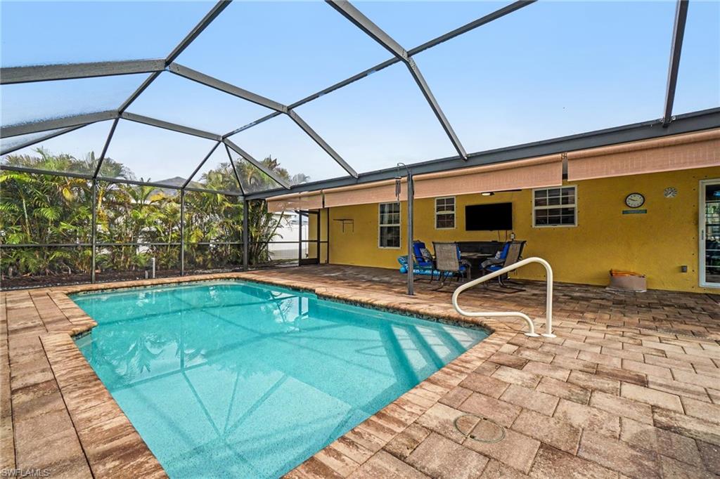 Screened-in pool area featuring a rectangular swimming pool, paver decking, a built-in television mount, and direct access to the interior
