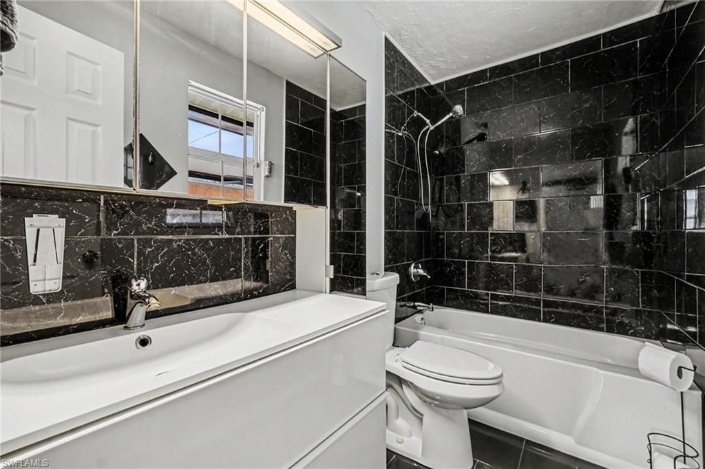 Black marble-effect tiled bathroom featuring a white vanity with integrated sink, chrome faucet, and a large mirrored medicine cabinet