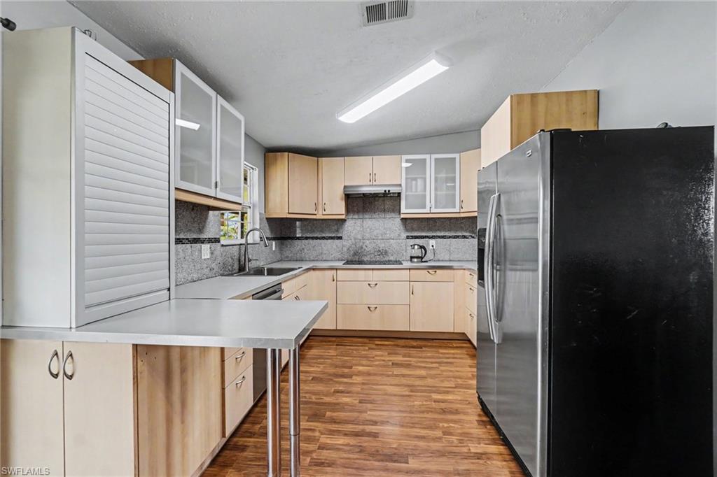 Open-concept kitchen featuring light wood-finish cabinetry, a stainless steel refrigerator, and a U-shaped countertop layout
