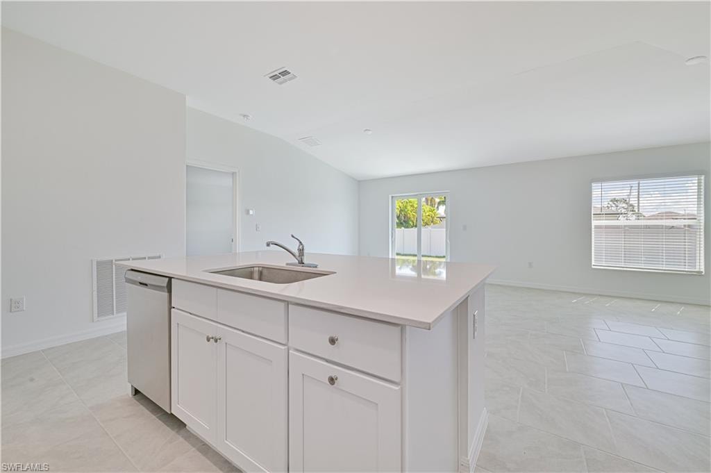 Kitchen featuring an island with sink, lofted ceiling, sink, stainless steel dishwasher, and white cabinetry