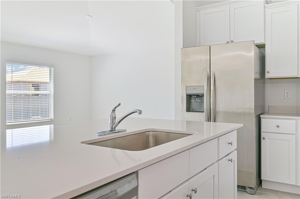 Kitchen with white cabinets, light tile patterned floors, white dishwasher, stainless steel refrigerator with ice dispenser, and sink