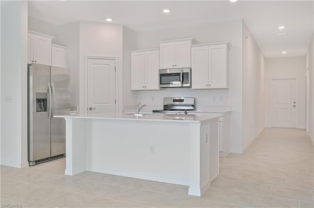 Kitchen featuring appliances with stainless steel finishes, white cabinets, light tile patterned floors, a kitchen island with sink, and sink