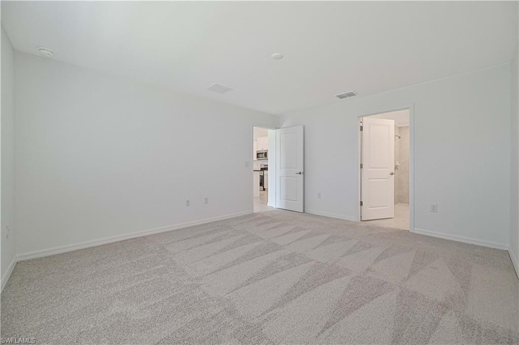 Unfurnished bedroom featuring connected bathroom and light colored carpet