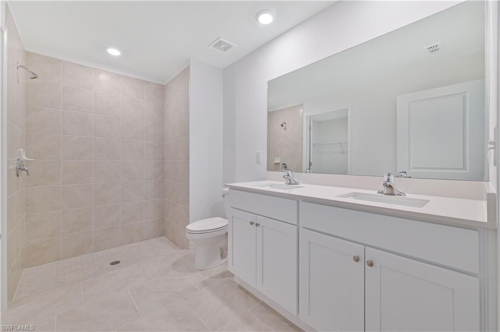 Bathroom with vanity, tile patterned floors, toilet, and tiled shower