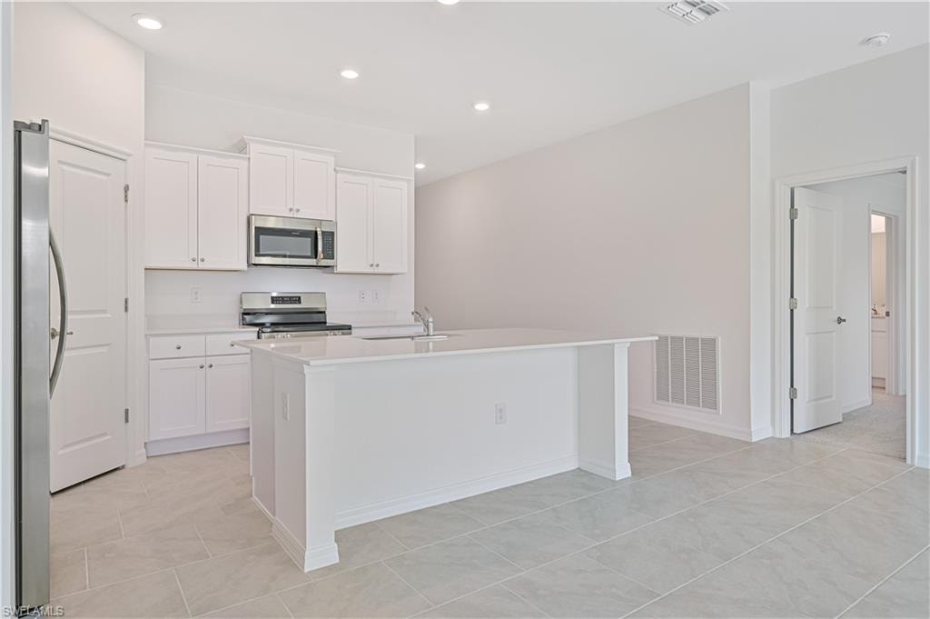 Kitchen featuring white cabinets, an island with sink, and appliances with stainless steel finishes