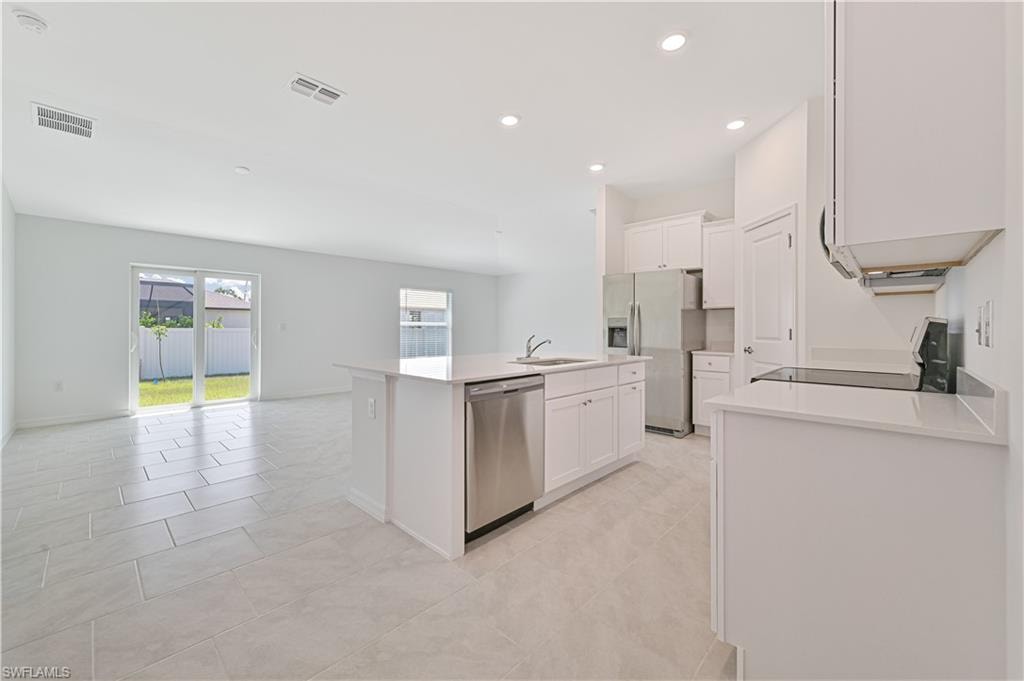 Kitchen with white cabinets, light tile patterned floors, stainless steel appliances, a kitchen island with sink, and sink
