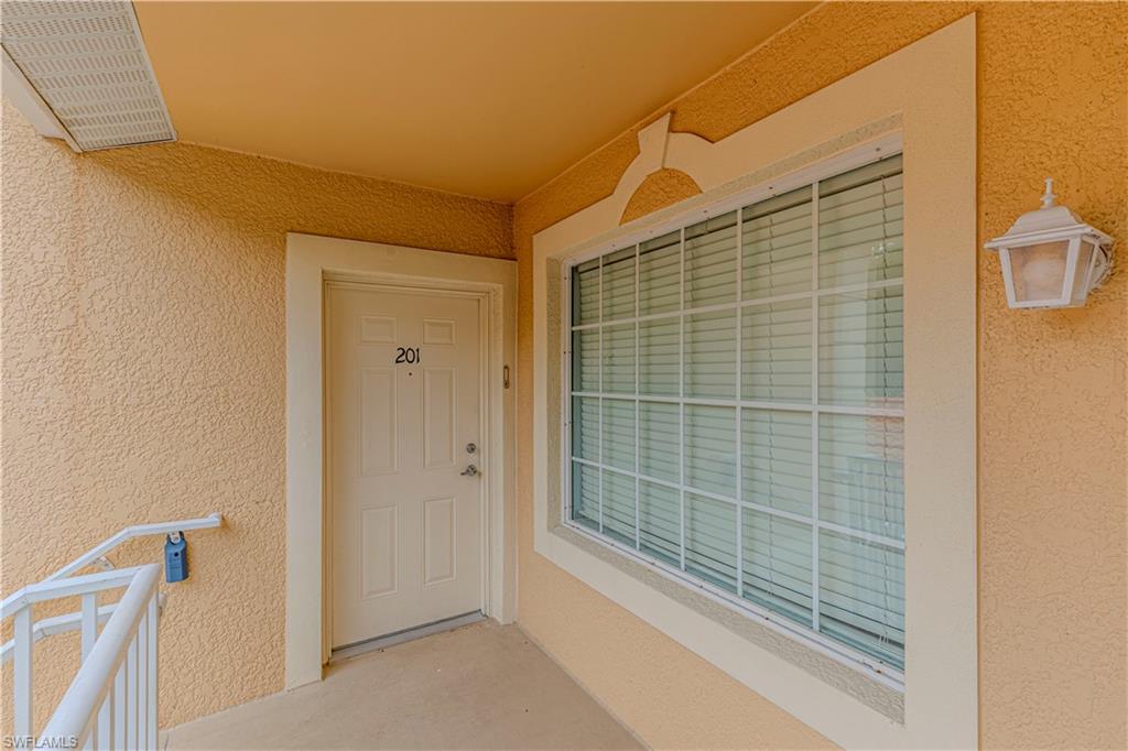Exterior entry featuring a number 201 door, an exterior wall sconce, and a multi-pane window with blinds