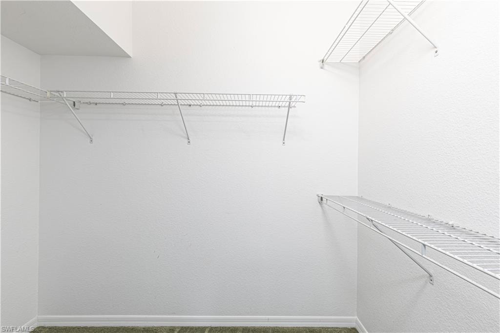 Walk-in closet featuring white wire shelving, white textured walls, and green carpet flooring
