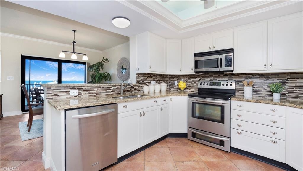 Kitchen with crown molding, stainless steel appliances, white cabinets, a peninsula, and decorative backsplash