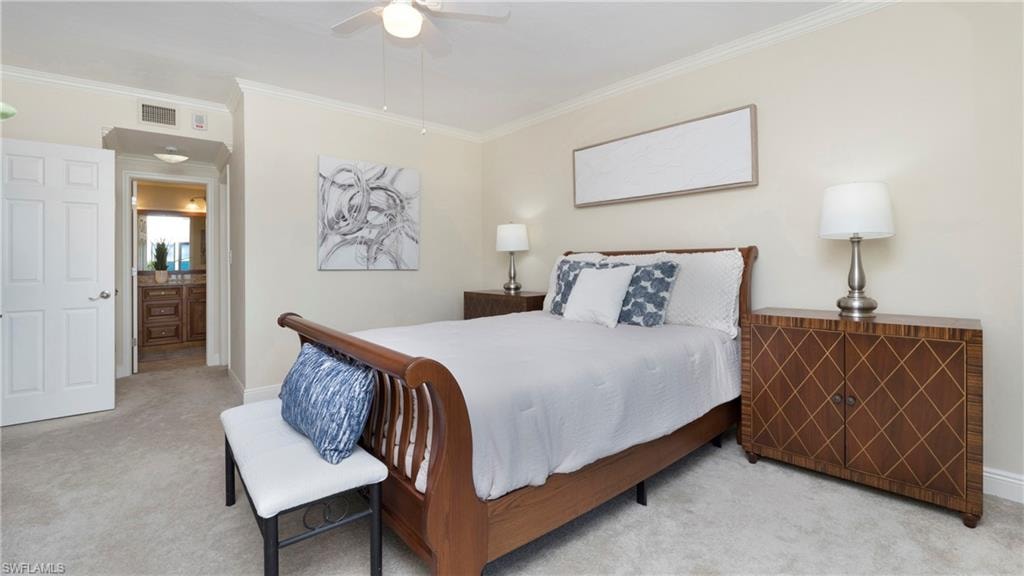 Bedroom with ornamental molding, light colored carpet, ensuite bathroom, and ceiling fan