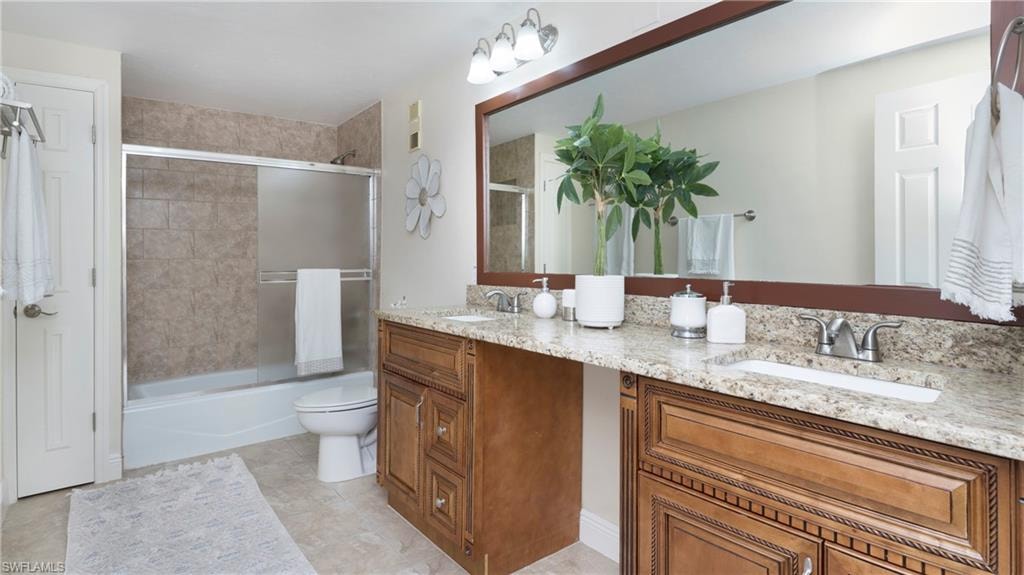 Full bathroom with shower / bath combination with glass door, double vanity, and light tile patterned floors