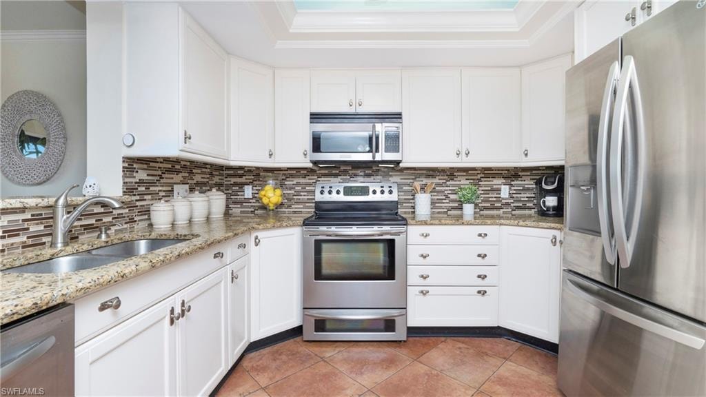 Kitchen featuring stainless steel appliances, white cabinets, backsplash, ornamental molding, and light stone counters