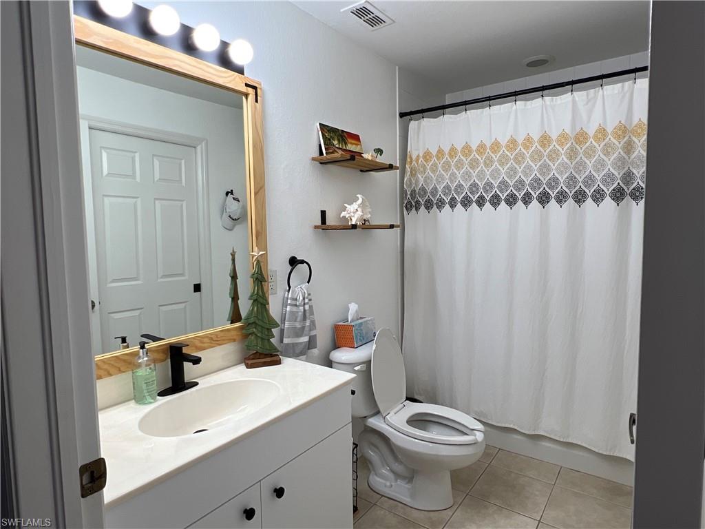 Bathroom featuring a white vanity with an integrated sink, a dark single-handle faucet, and a framed mirror with overhead vanity lighting