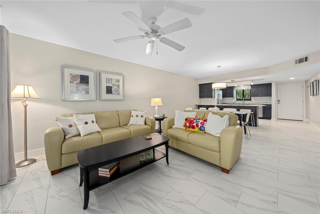 Open-concept living space featuring a ceiling fan, light-toned wall paint, and large format tile flooring