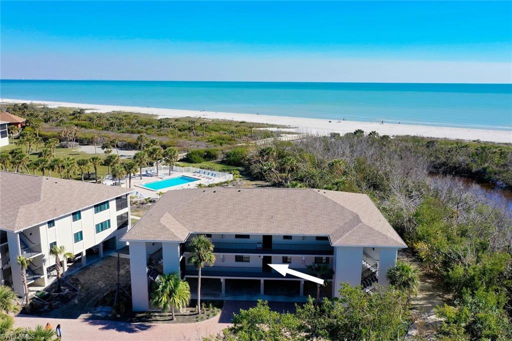 Coastal residential building featuring multiple levels and balconies, with a sandy beach and turquoise ocean visible in the background
