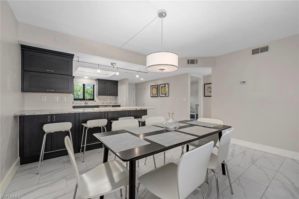 Open-concept dining area featuring light-toned flooring, a drum pendant light fixture, and a pass-through to the kitchen