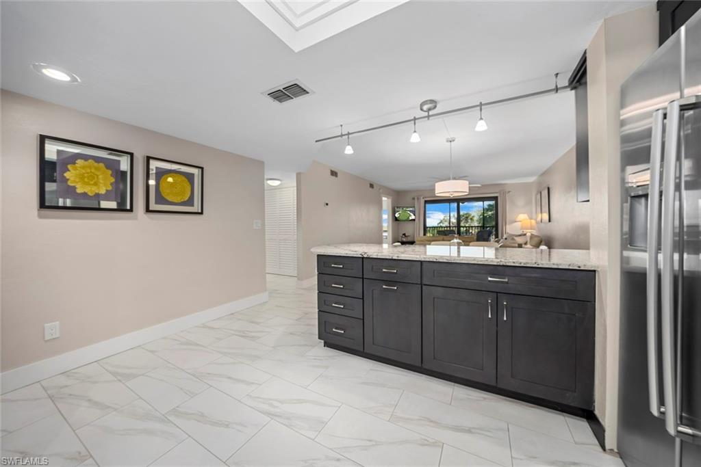 Kitchen island featuring dark cabinetry, light granite-style countertop, and stainless steel refrigerator