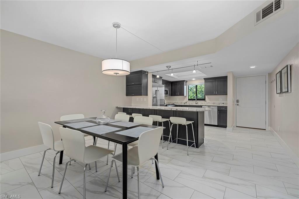 Open-concept living space featuring large format tile flooring, a contemporary drum pendant light, and a kitchen with dark cabinetry, stainless steel appliances, and a breakfast bar with stone countertops