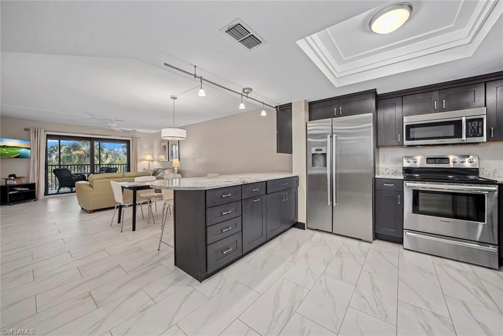 Open-concept kitchen featuring dark wood cabinetry, stainless steel appliances, a center island with a light-toned countertop, and tile flooring