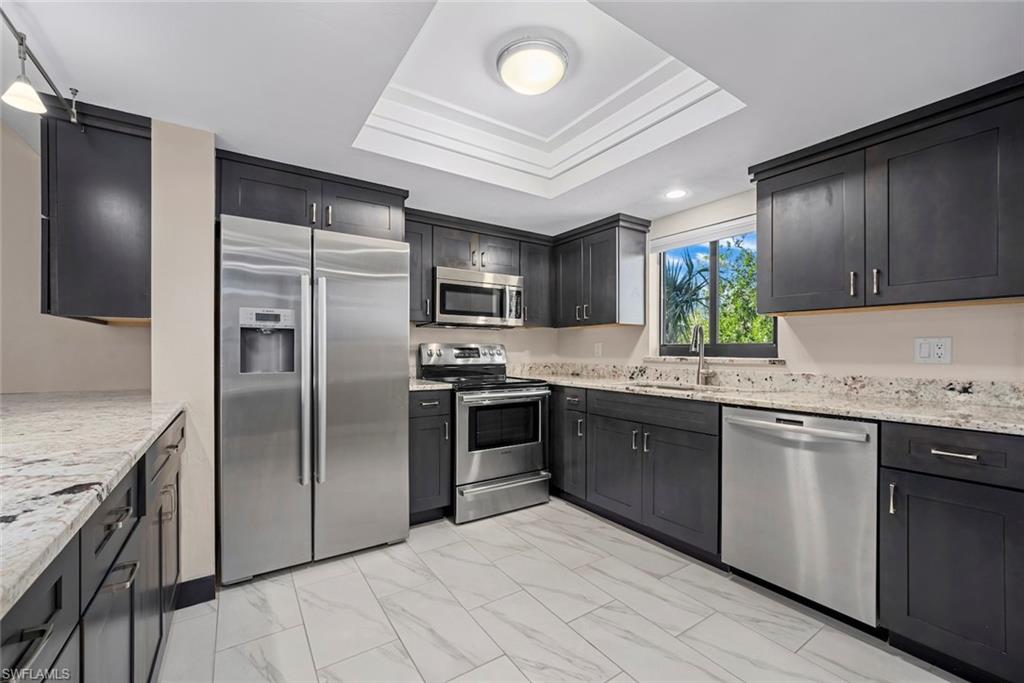 Kitchen featuring dark cabinetry, stainless steel appliances, light-toned countertops, and white tile flooring