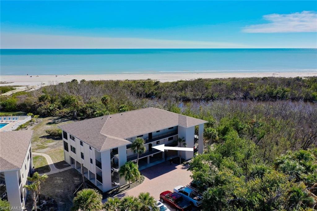 Coastal condominium building featuring multiple screened-in balconies, a paved drive, and surrounding natural foliage
