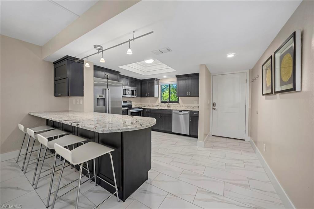 Modern kitchen featuring dark cabinetry, stainless steel appliances, and a light-toned granite countertop island