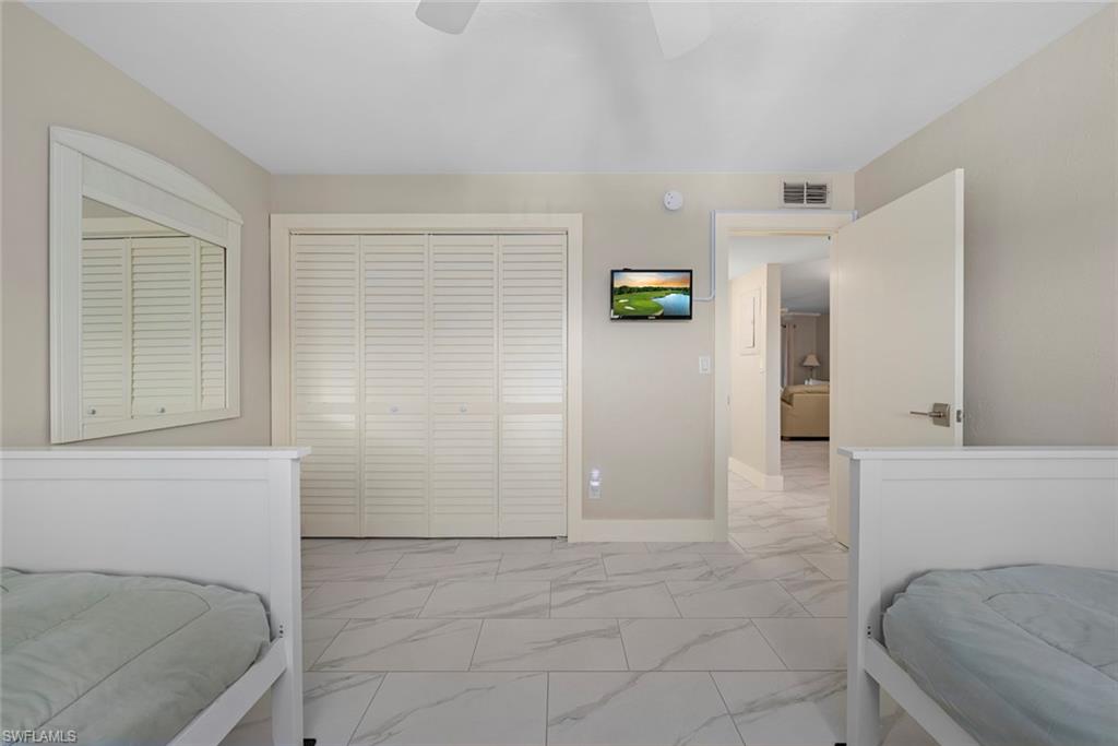 Light-toned room featuring a ceiling fan, louvered bi-fold closet doors, a wall-mounted television, and tile flooring