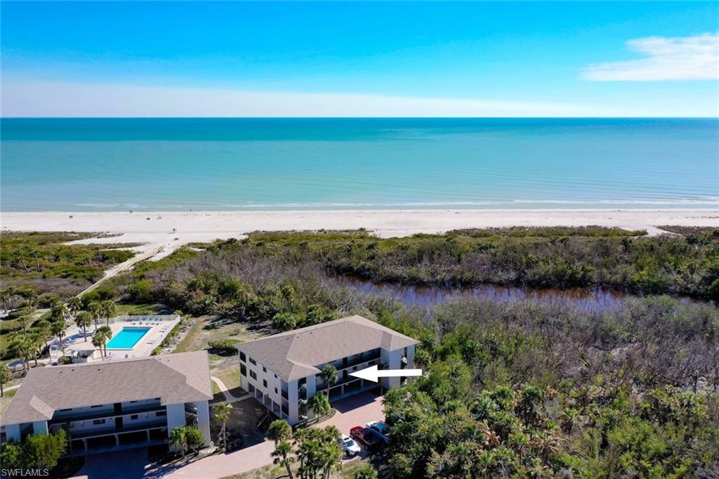 Coastal condominium community featuring multiple residential buildings, direct beach access, an outdoor swimming pool, and lush natural surroundings
