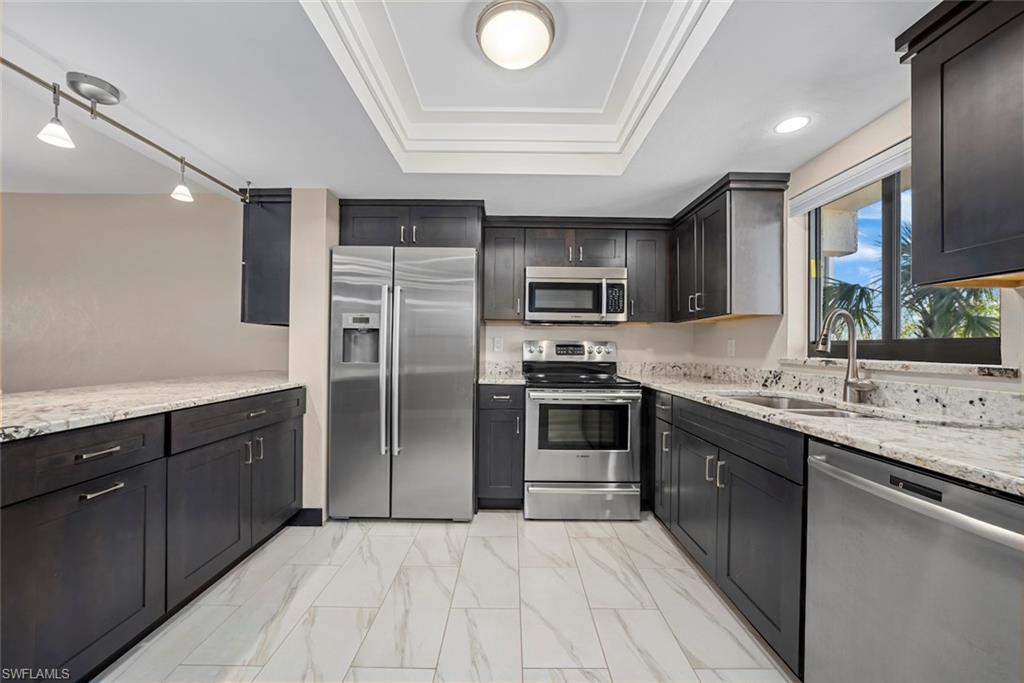 Contemporary kitchen featuring dark wood cabinetry, stainless steel appliances, and light granite-style countertops