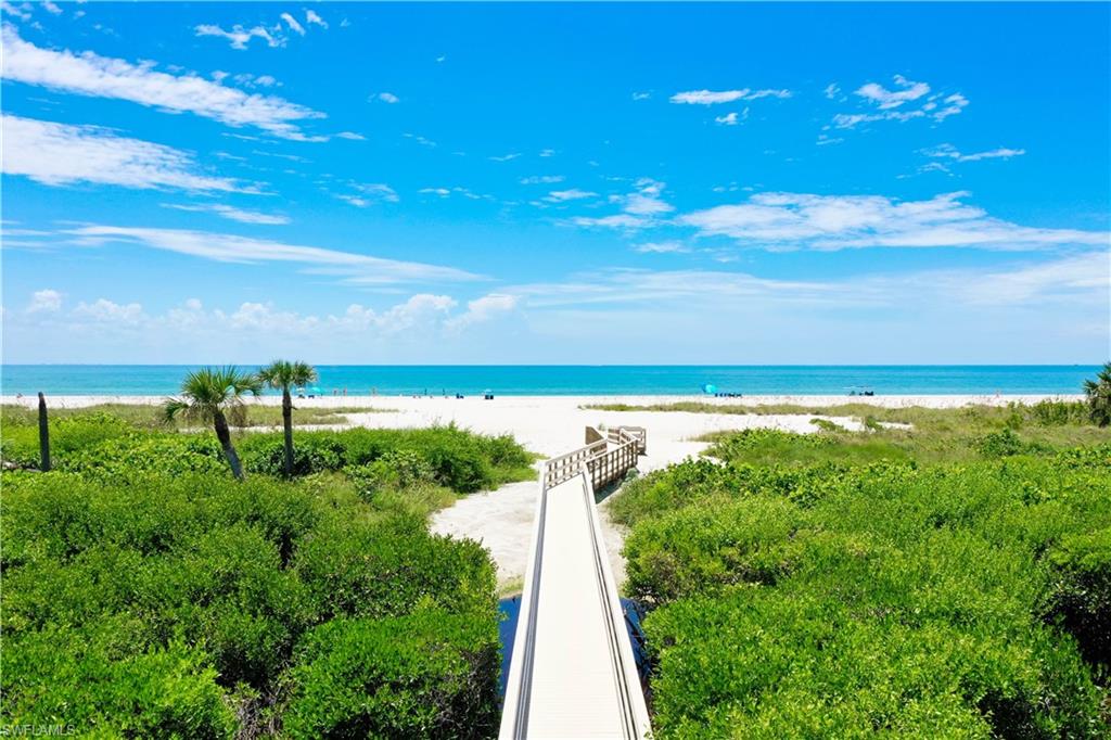Wooden boardwalk extending over lush green vegetation, leading to a white sand beach and the expansive blue ocean