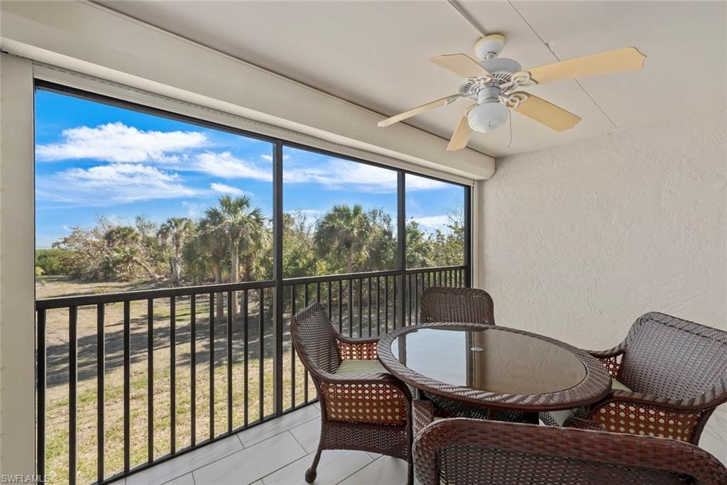 Screened balcony featuring a ceiling fan with light fixture, white tile flooring, and a privacy wall