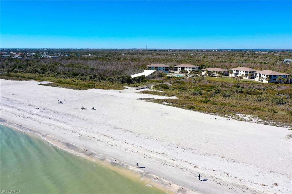 Expansive white sand beach with turquoise waters fronting a collection of multi-story buildings, surrounded by natural vegetation