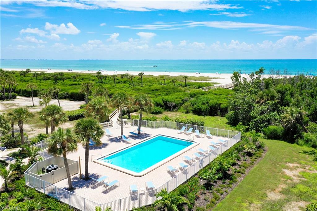 Fenced swimming pool surrounded by a paver deck with lounge chairs, mature palm trees, and lush landscaping